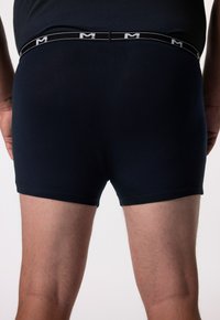 Caleçons boxers noirs en tissu lisse et extensible avec une ceinture élastique contrastante arborant un logo. La coupe est ajustée et épurée.