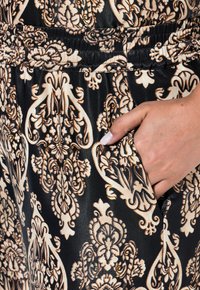 Zwarte stof met ingewikkelde beige bloemen- en abstracte patronen. Voorzien van een elastische tailleband en zijzak. Gladde textuur en glanzende afwerking.