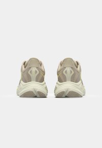 Beige athletic shoes with a textured upper, yellow accents, and a thick white sole. Rounded heel and supportive design for comfort.