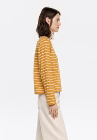 Gestreepte lange mouwen shirt in mosterdgeel met roze strepen. Zachte katoenen stof, relaxte pasvorm, ronde halslijn en een zoom die op de taille valt.