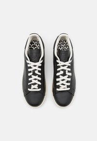 Pari mustia nahkakenkiä, joissa on valkoiset nauhat ja pohjat, kuvioidut mustavalkoiset sisäpohjat ja matala leikkaus.