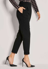 Vrouw in zwarte tapering broek met omslagen, een gestreept langemouwen shirt en zwart/beige hoge hakken met studs.