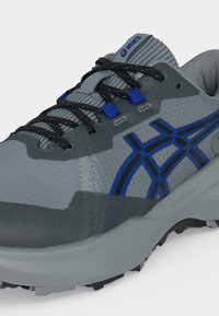 Γκρι και μπλε αθλητικά παπούτσια ASICS με μαύρα κορδόνια, ανθεκτικό διχτυωτό επάνω μέρος και υφή στην σόλα για πρόσφυση και άνεση.