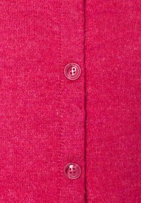 Fuchsia gestrickte Strickjacke mit weicher Textur, ausgestattet mit einer Reihe von fünf passenden pinkfarbenen Knöpfen auf der Vorderseite.
