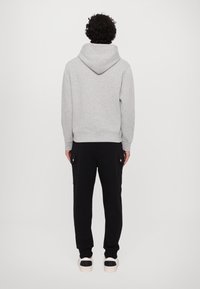 Felpa grigia con cappuccio e cordino, abbinata a pantaloni jogger neri con tasche laterali e bottoni a pressione.