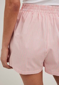 Rožinės ir baltos dryžuotos šortai su elastingu juosmeniu, turintys lygią tekstūrą ir šiek tiek siaurėjantį apatinį kraštą.