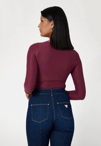 Burgundinės ilgos rankovės marškiniai derinami su aukštu liemeniu tamsiai mėlynomis džinsinėmis kelnėmis. Kelnėse yra dvi užpakalinės kišenės su baltomis siūlėmis ir mažas logotipas.