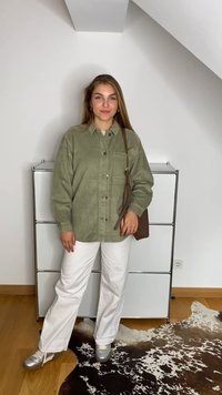 Camisola de cotim verde-oliva, calças brancas à boca de sino e sapatilhas prateadas. Bolsa castanha com alça ajustável. Fundo simples.