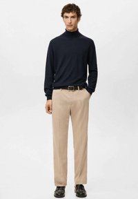 Marineblauwe coltrui gecombineerd met beige broek, met een rechte snit, gladde stof en een bruine leren riem met een eenvoudige gesp.