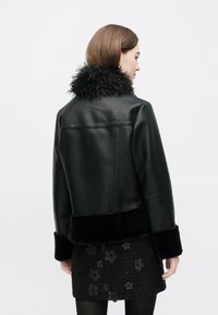 Svart skinnjacka med texturerad svart fuskpälskrage och muddar, kort design och slät finish, bärs över en svart kjol med blommönster.