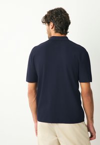 Tengerészkék rövid ujjú galléros póló, texturált anyagból, lapos gallérral és kényelmes szabással. Egyenes szegéllyel és letisztult részletekkel.