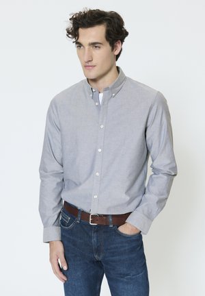 Camisa gris abotonada con un pequeño cuello, combinada con vaqueros azul oscuro y un cinturón de cuero marrón. Tela suave, diseño casual.