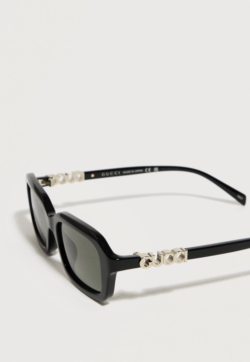 Black rectangular sunglasses with dark lenses and metallic gold "GUCCI" logo on the temples, shown against a white background.