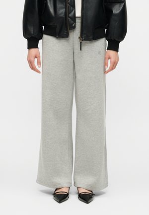 Modelka ubrana w jasnoszare szerokie spodnie dresowe, czarne baleriny z zaostrzonym noskiem oraz czarną skórzaną kurtkę zapinaną na pół.