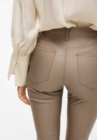 Slim-fit, visok pas bež hlače z gladko teksturo, s hrbtnimi žepi in šivanim šivom. V kompletu z svetlo obarvanim zgornjim delom.