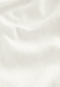 Mäkká, biela, mierne textúrovaná látka s jemnými záhybmi a subtilným vzorom tkania zobrazená zblízka.