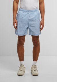 Shorts de sport bleu clair en tissu texturé, avec une taille élastique et un petit patch logo en bas à gauche.