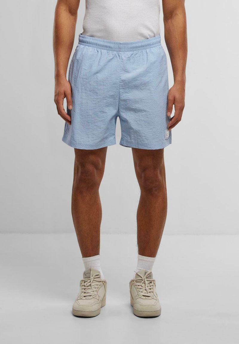Shorts de sport bleu clair en tissu texturé, avec une taille élastique et un petit patch logo en bas à gauche.