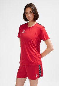 Completo sportivo rosso composto da maglietta e pantaloncini realizzati in materiale leggero, con scollo a V, logo sul petto e dettagli laterali blu a contrasto.