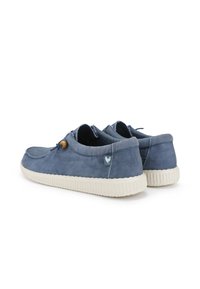 Blue canvas slip-on shoes with a textured finish, white rubber sole, and wooden accent on the lace. Features a small logo on the side.