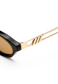 Γυαλιά ηλίου με μαύρο πλαίσιο, ορθογώνιους κεχριμπαρένιους φακούς και χρυσά μεταλλικά μπράτσα με μια εγκοπή και τρεις διαγώνιες ραβδώσεις κοντά στον μεντεσέ.