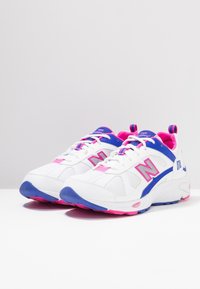 Bílé sportovní tenisky s modrými a růžovými akcenty, síťovina, kulatá špička, texturovaná podrážka a vzorované tkaničky. Modelové číslo 876 na boku.