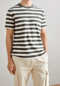 Hombre que lleva una camiseta de rayas horizontales gris y blanca de mangas cortas y pantalones cargo beige con bolsillos laterales.