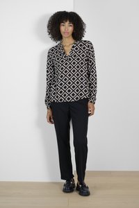 Schwarz-creamfarbene Bluse mit diamantförmigen Mustern, entspannte Passform, lange Ärmel, kombiniert mit schwarzen Hosen und klobigen schwarzen Schuhen.