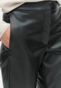 Zwarte neplederen broek met een gladde textuur, voorzien van zijzakken en een op maat gemaakte pasvorm, benadrukt door subtiele naden en stikdetails.