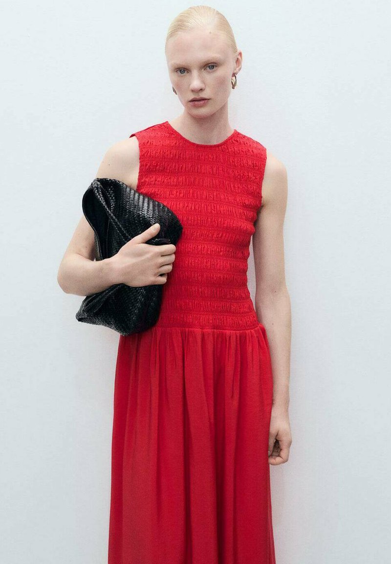 Robe rouge sans manches avec un corsage froncé et une jupe fluide, accompagnée d'une pochette noire texturée. Design simple et élégant.