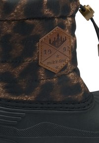 Botte à motif noir et marron avec une tige en tissu texturé et une partie inférieure en caoutchouc, dotée d'une pièce de cuir marron avec logo et d'une fermeture à bouton-poussoir.