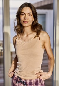 Beige bomulds tank top med en rund udskæring. Sammen med ternede pyjamabukser med et bånd til snøringen. Modellen står med hænderne i lommerne.