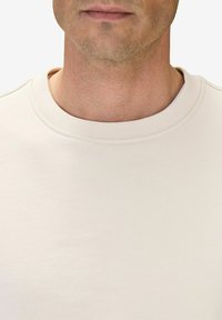 Ljusbeige sweatshirt med rund halsringning, i mjukt bomullsmaterial och med minimala sömmar, som visar upp en enkel och ren design.