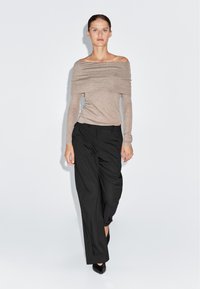 Top beige a spalle scoperte con maniche lunghe, abbinato a pantaloni neri a gamba larga e décolleté nere a punta. Tessuto liscio e leggero.