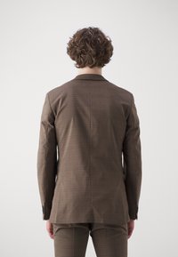 Sacou cu carouri maro, cu o croială ajustată, având o deschidere unică, rever cu fason clasic și manșete cu nasturi. Textura materialului este netedă.