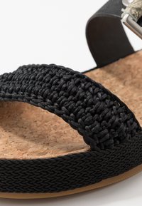 Black braided strap sandal with cork footbed and rubber outsole. Features a woven texture and metallic buckle detail on the strap.
