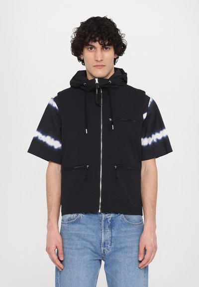 Veste noire à manches courtes avec capuche, présentant un motif tie-dye sur une manche, fermeture éclair et deux poches avant. Texture de tissu lisse.