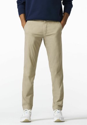 Beige katoenen chinos met een toelopende pijpdesign. Beschikt over zijzakken en een soepele textuur, gecombineerd met witte sportschoenen.