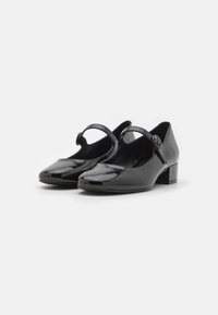 Black patent leather Mary Jane shoes with a low block heel, single strap, and rounded toe. Smooth texture with a shiny finish.