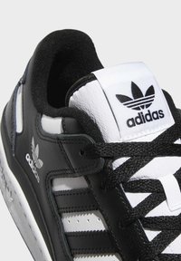 Close-up of black and white Adidas sneaker with black laces, Adidas logo on the tongue, and three black stripes on the side.