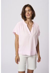 Blouse en lin rose clair avec des manches courtes, col en V sans boutons, et plis subtils aux épaules, assortie à un short blanc. Texture lisse.