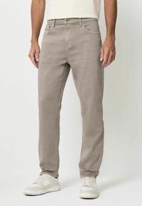 Kerged helepruun denimipüksid, millel on kitsas lõige, esitatud ees- ja tagataskutega, kombineerituna valgete tossudega, et saavutada lõdvestunud välimus.