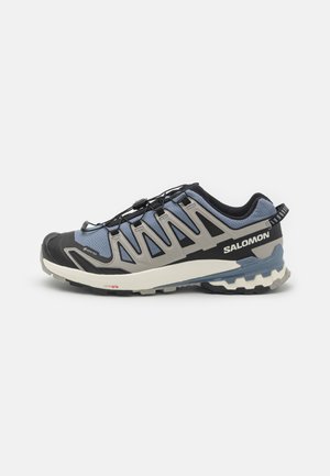 Zapatillas de trail Salomon con parte superior de malla azul y gris, puntera de goma negra y plantilla blanca. Presentan un sistema de lazado rápido y suela texturizada.