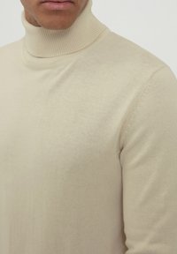 Beige Rollkragenpullover aus glattem Strickstoff. Mit einem gerippten Hals und dezenten Stichdetails an der Schulter. Figurumspielende Passform.