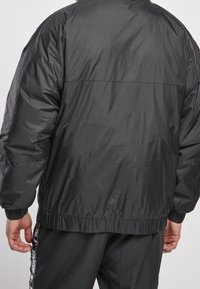 Black puffer jacket with a smooth, shiny exterior. Features elastic cuffs and hem, relaxed fit, and no visible logos or patterns.