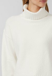 Weißer, strukturierter Rollkragenpullover mit geripptem Kragen und überschnittenen Schultern. Weiches, gemütliches Material mit einem glatten, samtigen Aussehen.