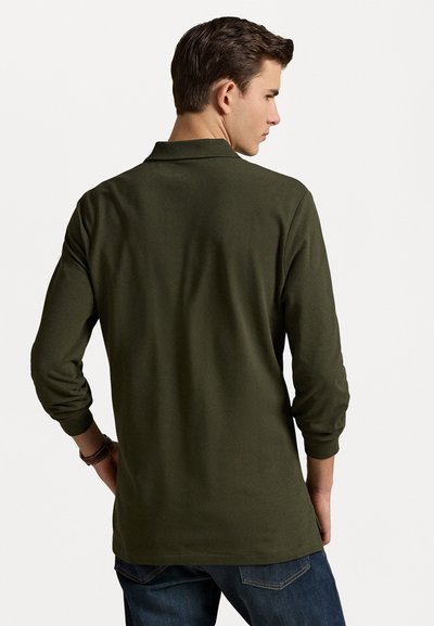 Cămașă polo verde măsliniu cu mâneci lungi, cu guler, având o textură netedă și un design ajustat, asortată cu blugi.