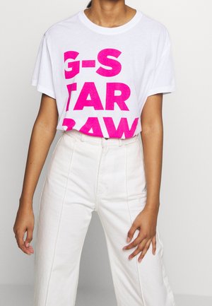 Biała bawełniana koszulka z wyboldowanym różowym napisem "G-S TAR RAW" na przedzie. W zestawie z białymi dżinsami z wysokim stanem.
