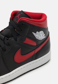 Juodųjų odinių aukštų sportbačių su raudonais akcentais, kuriuose yra raudona Nike swoosh ir Air Jordan logotipas šone. Raižytos juodos šniūrelės.