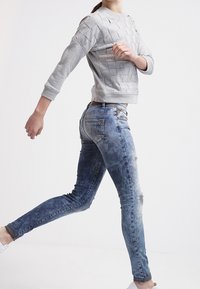 Suéter gris texturizado de diseño amplio, combinado con jeans ajustados azul oscuro con un acabado desgastado y lavado claro. Zapatillas blancas.
